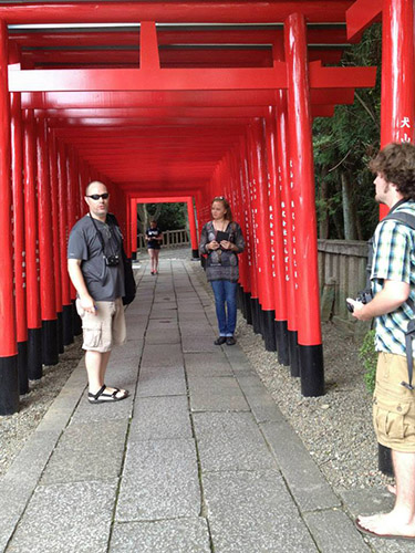 Author underneath a row of torii; one student stand near him and another standing just before the threshold