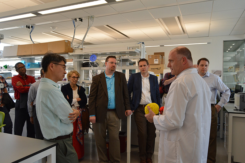 A group of people standing in a lab listening to scienctist speak.