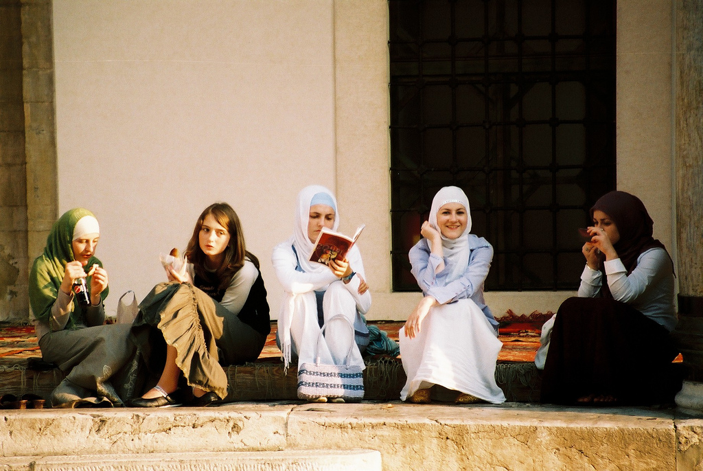 Five women sitting on stairs outside a building in Sarajevo chatting. Four are veiled, and one is reading a book.