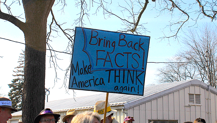 A protest sign reads "Bring Back Facts! Make America THINK again!"