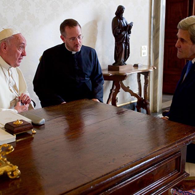 Former US Secretary of State John Kerry sits with Pope Francis and his translator on December 2, 2016 in the Vatican. They sit around Pope Francis' desk.