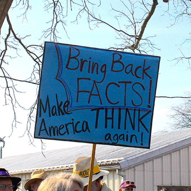 A protest sign reads "Bring Back Facts! Make America THINK again!"