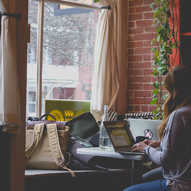 woman working on a laptop faces the window inside a coffee shop