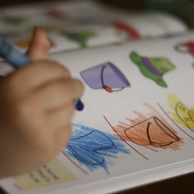 child's hand with a crayon coloring line images of hats in many colors